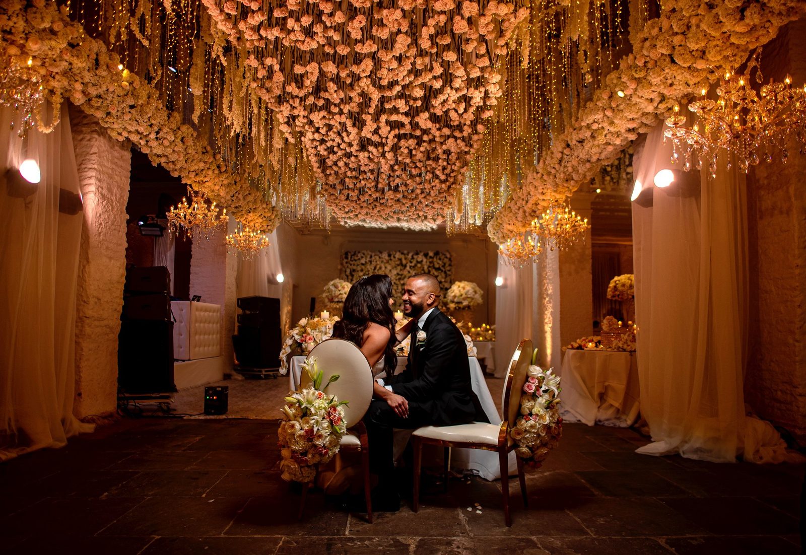 Couple under a hanging ceiling of pink flowers at a candlelit reception in Cartagena
