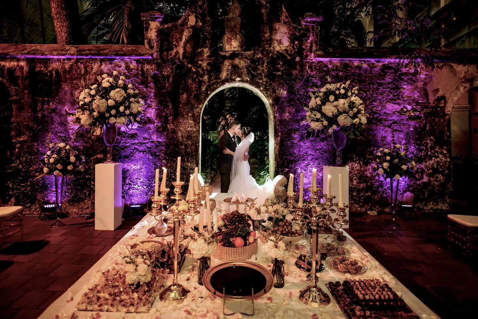 Reception with violet lighting and a floral arch in a stone courtyard