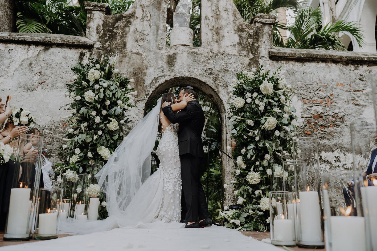 Couple kissing under a stone arch decorated with white flowers and candles