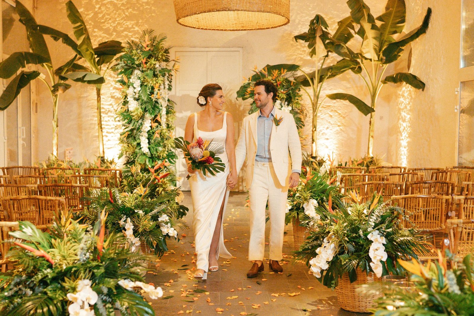 Bride and groom walking down a tropical aisle with heliconias and palms