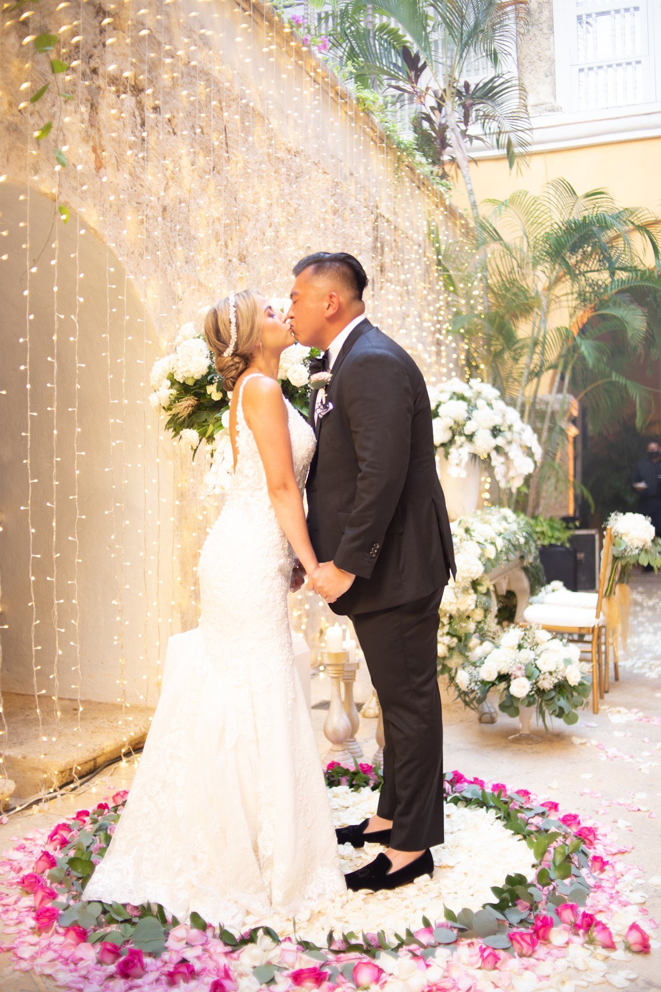 Couple kissing under a floral arch surrounded by pink flowers