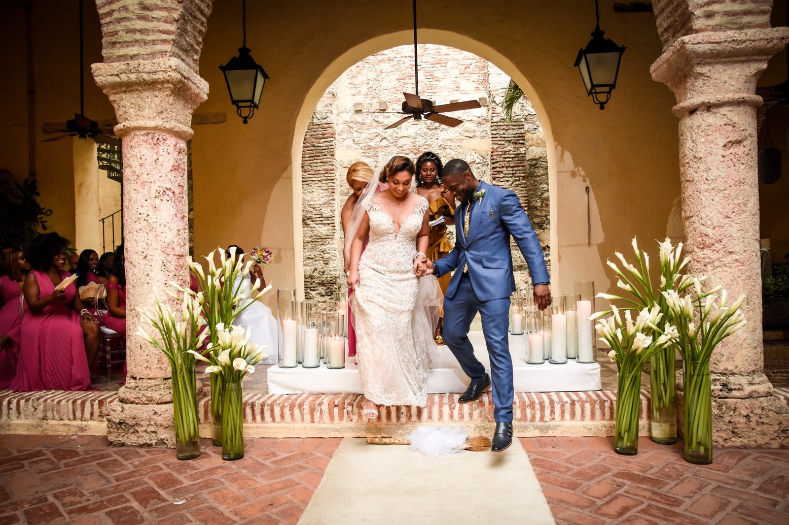 Couple jumping the broom at the end of a candlelit ceremony in a colonial courtyard