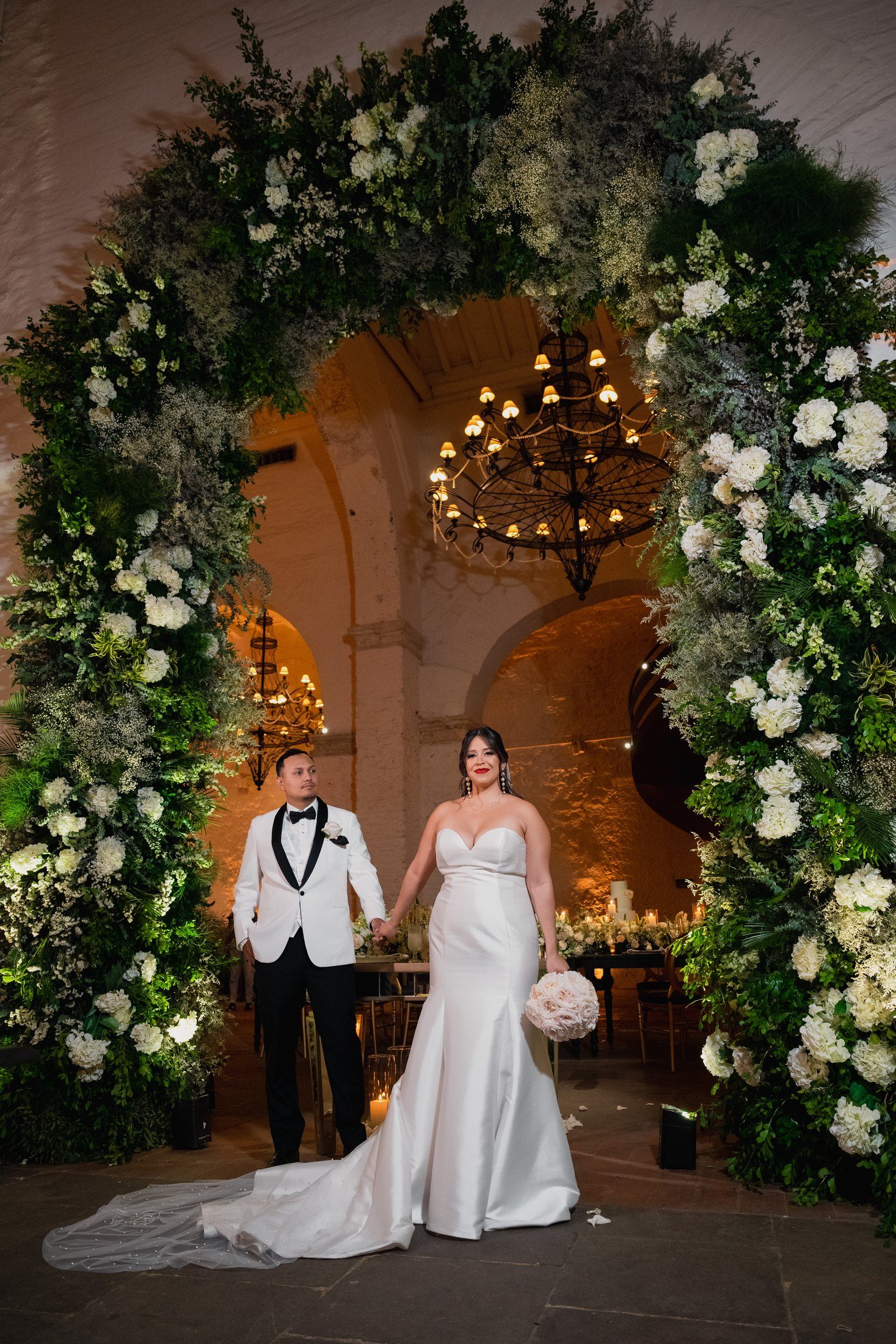 Couple under a white floral arch in a colonial courtyard